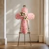 Pink floral cross arrangement on a stand with a ribbon bow