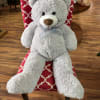 Large gray teddy bear with a ribbon bow sitting on a patterned chair
