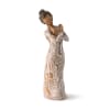 Faceless figurine of a woman in a long brown dress with white decorative patterns, arms crossed over her chest