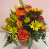 Mixed bouquet of orange roses, yellow daisies, and lilies in a vase
