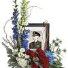 Floral tribute around a framed military portrait with red, white, and blue flowers