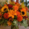 Autumn bouquet with orange lilies, roses, sunflowers, and chrysanthemums in a glass vase