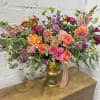 Large mixed bouquet in a gold vase with pink, orange, and purple flowers