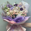 Bouquet of pastel orchids, roses, and purple blooms wrapped in lavender paper