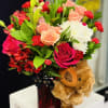 Bouquet of pink, peach, red, and white flowers with a teddy bear