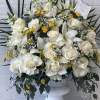 White roses and lilies in a white pedestal vase with yellow accents