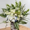 Tall arrangement of white orchids, roses, lilies, and green orchids in a rustic cylinder vase