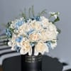 Cream roses and blue filler flowers in a black hatbox