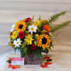 Mixed bouquet with sunflowers, daisies, and red carnations in a patterned vase