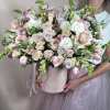 Large pastel arrangement of roses, tulips, and orchids in a blush hatbox held by a person