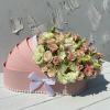 Pink carriage-shaped box filled with cream and blush roses and lisianthus, trimmed with a white bow and pearls