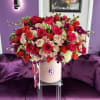 Large hatbox arrangement of red, hot pink, and cream roses with orchids in a blush pink box.