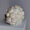 Round hand-tied bouquet of ivory peonies resting on a white pedestal