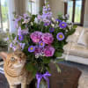 Purple bouquet in a glass vase beside an orange tabby cat