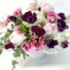 Pink and white bouquet with dark purple blooms in a white vase