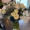 Bouquet of cream roses, white blooms, and blue thistles in a glass vase