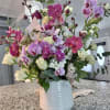 Tall arrangement of pink and purple orchids with white roses in a white ceramic vase