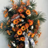 Tall standing spray with orange gerbera daisies, white flowers, palm fronds, and a Harley-Davidson logo sign.