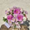 Pink gerberas and daisies arranged in a clear glass vase with a ribbon.
