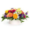 Low arrangement of bright mixed flowers in a white round vase