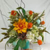 Orange and white floral arrangement in a turquoise vase with decorative branches