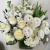 White roses and ranunculus in a glass vase with white filler flowers