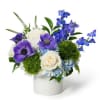 Compact blue and purple flower arrangement with white roses in a white ceramic cylinder vase