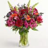 Bouquet of red roses, pink alstroemeria, and orange daisies in a clear glass vase