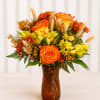 Orange and yellow flower arrangement in an amber glass vase