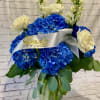 Blue hydrangea and white rose arrangement in a glass vase with a white ribbon