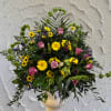 Mixed bouquet with pink roses, yellow daisies, and purple accents in a white vase