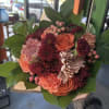 Handheld bouquet of orange and burgundy flowers with large green leaves