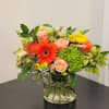 Mixed bouquet with orange gerbera daisies, peach roses, and green hydrangea in a glass vase