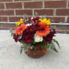 Mixed bouquet in an amber glass pumpkin vase with orange, yellow, burgundy, and white blooms