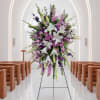 Tall floral spray with white lilies and purple blooms on a stand in a church aisle