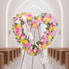Heart-shaped floral wreath with pink and yellow roses on a stand