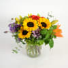 Mixed bouquet with sunflowers, roses, and lilies in a clear glass vase