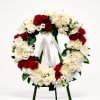 Circular wreath of red and white flowers on an easel with a white ribbon