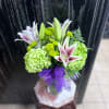 Bouquet of green hydrangeas and white lilies with a purple ribbon in a glass vase