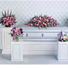 Pink and purple funeral floral sprays around a silver casket