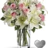 Pink roses and white lilies in a clear glass vase with a heart keepsake