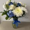 White roses and blue flowers arranged in a glass vase with a blue ribbon.