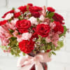 Red roses and pink flowers in a vase with a pink ribbon