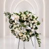 White floral wreath with roses and ribbon on a stand