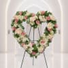 Heart-shaped floral wreath with pink roses and pale hydrangeas on a stand