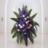 Tall purple and white floral arrangement with fern fronds and blue ribbon