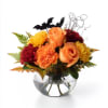 Orange and red floral arrangement in a clear glass bowl with bat decorations