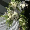 White floral standing spray on an easel beside a mannequin and draped fabric