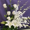 White roses, lilies, and orchids arranged in a tall vase