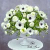 White anemones and ranunculus arranged in a white pedestal vase